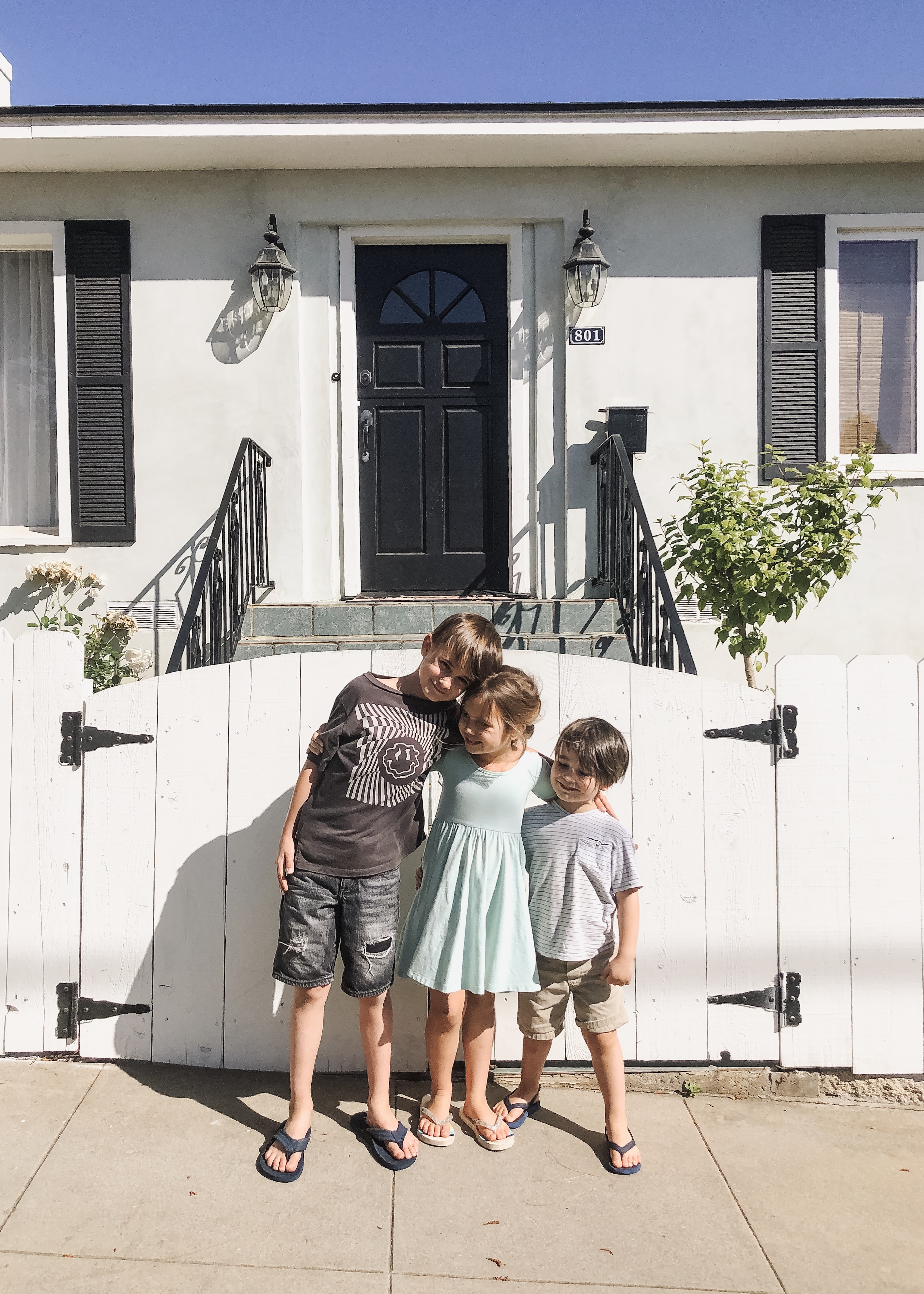 three kids standing in front of a white picket fence